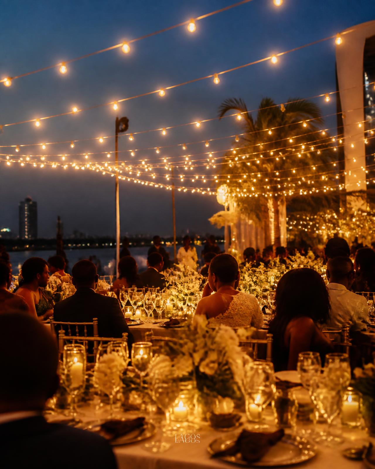 Outdoor evening celebration under string lights with candlelit banquet tables